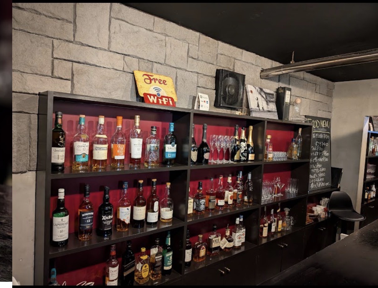 BAR REALTAの赤い背景の酒棚に並ぶウイスキーなどのボトルとグラス