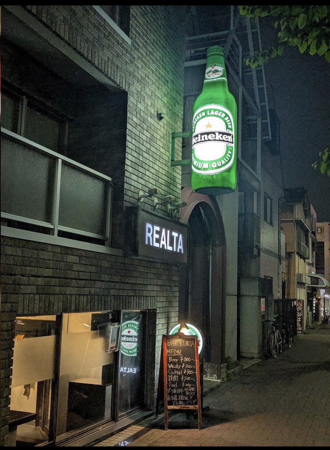 BAR REALTAの夜の外観。REALTAの看板と緑のボトル型看板、建物1階のガラスの入口